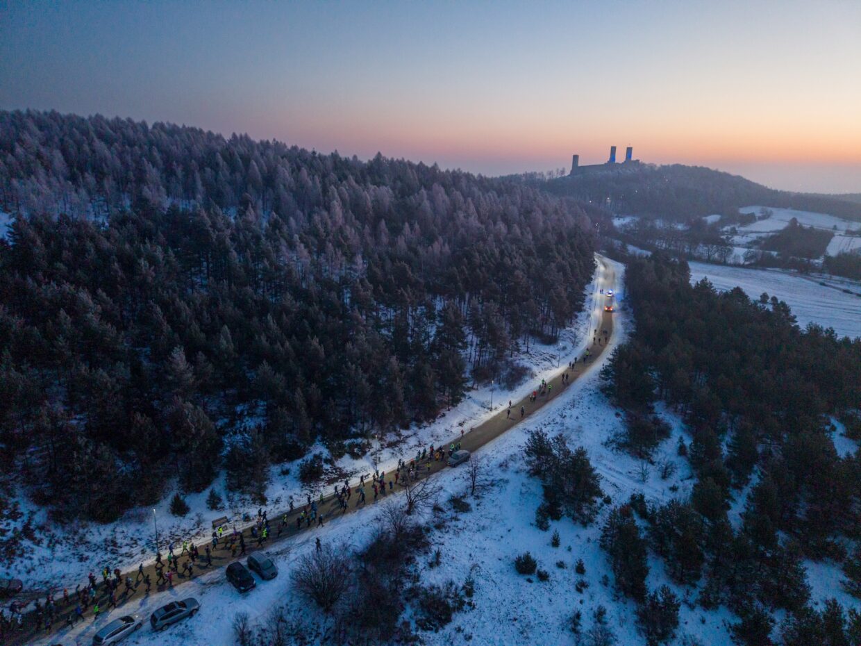 Widok z drona na dużą grupę uczestników maratonu, w tle widać Zamek Królewski w Chęcinach na tle różowego nieba.