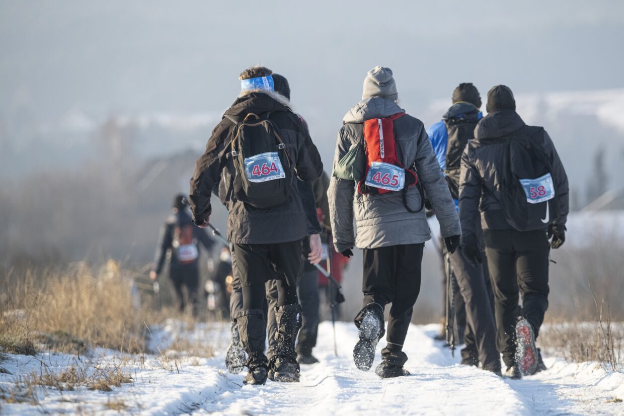 Zdjęcie grupy piechurów na trasie maratonu. Widoczne są ich plecaki oraz numery startowe.